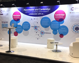 Exhibition stage for Cancer Research UK complete with chairs, stools, tables and a visually informatative backdrop.